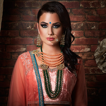 Bride wearing a peach lengha and green jewellery looking straight forward